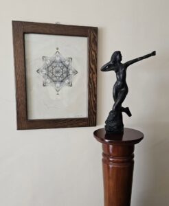 Cuadro de geometría en tinta en pared con fonso color netro y una escultura en bronce que decoran un espacio de cliente.